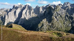 A drone flies out from behind a mountain, revealing a fantastic panorama of rocky mountain peaks illuminated by the sun