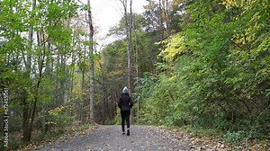 woman walking on a hiking trail in Taughannock Falls State Park (waterfall near Ithaca, finger lakes region of upstate new york) cascade, gorge, autumn, jacket, hat, fall foliage shot from behind