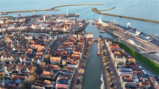 High aerial arc around the harbor entrance and town from an angled overhead perspective.