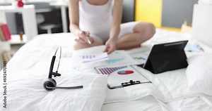 Person sits on bed and studies financial analytical charts. Telework and remote work as marketer concept