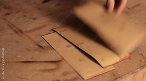 Laying down different types of sandpaper with different levels of grit face down on a wooden surface