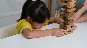 Cute Asian siblings having fun playing Jenga together. Two children playing Jenga board game on table in room at home. Wooden puzzles are games that increase intelligence for children.