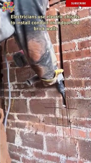 Electricians use electric chisels to install conduit on indoor red brick walls