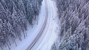 Aerial flight over winter forest with road. Snowy tree branch in a view of the winter forest. Aerial footage, 4K
