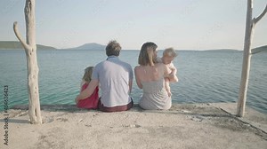 Slow motion - Couple kisses while sitting on the dock with their two kids. Young family with small children enjoying their vacations at the sea