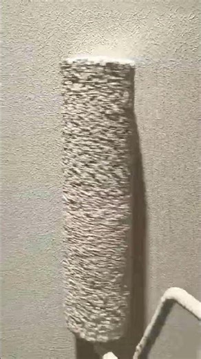 applying a thick layer of textured paint to a wall using a specialized roller for a uniform finish
