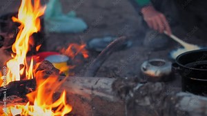 Yukon Territory, Alaska. Night camp of a canoe expedition to Alaska. Camp fire burning while adventurer prepares mash potatoe in the background.