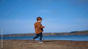 Lovely toddler boy walking to the river. Cute little kid throws the stone into water and walks away.