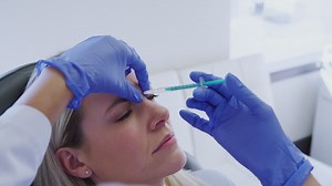 Premium stock video - Woman sitting in chair being give botox injection between eyes by female doctor