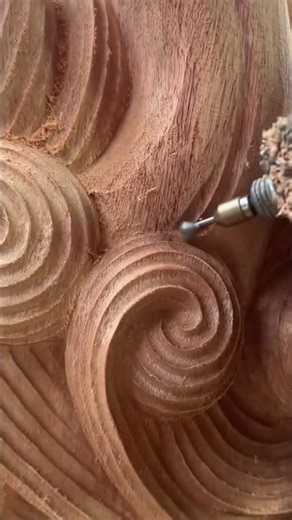 carving circular spiral patterns on a large wooden sculpture surface using a small rotary power tool