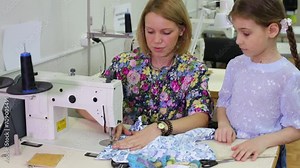 tailor sits at table with sewing machine and shows seam to girl