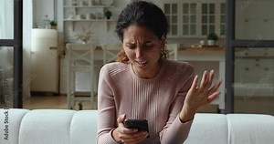 Confused young woman looking at mobile phone screen, feeling stressed of getting message with unpleasant scam news. Unhappy millennial caucasian lady dissatisfied with bad smartphone device work.