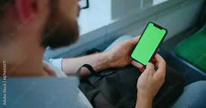 Back shot of young man holding mobile phone with vertical green screen. Background of tram window, key smartphone, touch message display, close up. City lifestyle. New modern gadgets technologies.