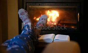 Woman in pyjamas by the fireplace, reading a book. Winter, winter holidays, leisure time at home, and relaxation. Winter vacation at home and Christmas.