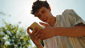 Cheerful Hipster Guy chatting on Social Media using Modern Smartphone. Standing on city street, Typing Message. Attractive smiling Mixed Race Male with a Stylish Haircut. Browsing Mobile Phone.