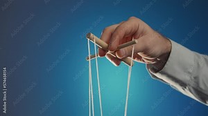 The hand of a man in a gray shirt controls a puppet using a wooden manipulator and strings on a blue background. Hand handling at puppet by pulling strings to make the character move. Close up.