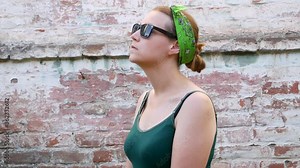 Woman with pollen allergy symptom smelling air with nose standing on brick wall background. Young sick girl sneezing, blowing her nose into handkerchief, using nasal spray against allergic rhinitis.