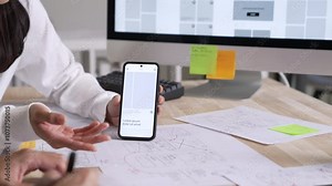 UX UI designer testing prototype on a phone, discussing and brainstorming on wireframes for a website and mobile app prototype, in the concept of website and mobile application design concept.