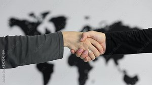 Handshake of two men near black world map on white wall