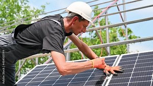 Worker mounting photovoltaic solar panel system outdoors. Man engineer tightening solar module on metal rails with hex key, wearing construction helmets and work gloves. Stock Video