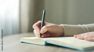 close-up of a female hands taking notes in a notebook notepad using pen on modern desk at home young woman writes in a diary with a pen while sitting at the table Close up commonplace
