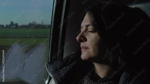 Female passenger asleep by train window while traveling. Woman commuter napping while landscape passes by in background