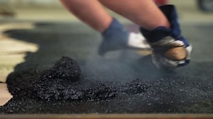 Manual workers lay a new asphalt coating on ground using hot bitumen with tar at construction site - hands close-up | Premium Stock Video Footage