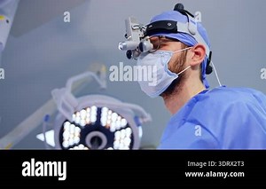 Kyiv, Ukraine, 9 August 2025: Surgeon wearing binocular loupes and headlight in operating room. Portrait of male doctor in surgical mask and blue cap with magnification loupes Stock Video Footage - Alamy