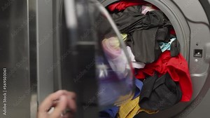 Man pushing dirty clothing into a front loading of washing machine then can not closing the door because it is full.