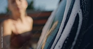 A woman washes a car with a foam washcloth in the yard at home. Cleanliness of private car washing from dirt for the trip. High quality 4k footage