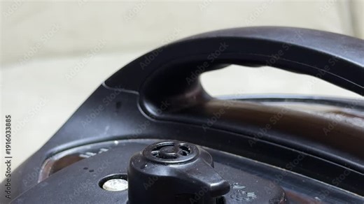 The steam release valve on a pressure cooker lid is turned to the venting position. High-pressure steam escapes through the nozzle, creating a sharp, continuous hissing and whistling sound.