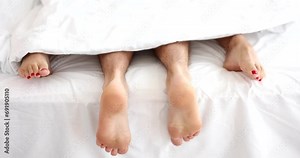 Married couple in comfortable bed makes love. Male and female legs in bed top view