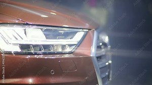 closeup side view of a working headlight of a new luxury car / spotlight headlamp elegant exclusive auto exhibition show business presentation tuning nobody automobile industry detail rays light beam