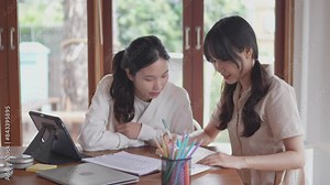 Two Asian university female friends are studying together by discussing the course content and solving statistics problems using a calculator, feeling happy when they solve problems correctly at home