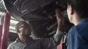 Low angle view of car specialist examining breakdown cause of car bottom together with male client
