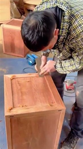Craftsman hand planing the surface of a wooden cabinet in a workshop