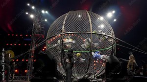 A dangerous stunt show with motorcyclists in a circus. Six stunt actors ride motorcycles in a metal round cage at a circus performance, a dangerous stunt. Coverage of a concert at a circus performance