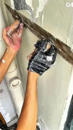 Trowel smooths plaster—wall transforms beneath steady strokes and renovation grit