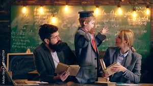 A boy in a jacket and graduation hat communicates with two teachers who hold books in the background of the school class. Learning concept. School children in uniform. Teacher in classroom.