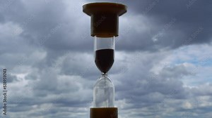 Timelapse hourglass on blue clouds background. Time is running out. The sand in the clock is pouring and fluffy clouds are floating.