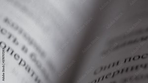 Printed lines of text consisting of words with black letters on pages of hardcover book made of white paper on fold of textbook fast movement of camera from top to bottom with variable focus close up