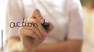 A girl writes action time on glass with a black marker.