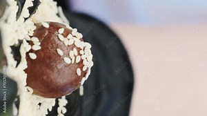 Hand in latex glove holding chocolate ball-shaped candy. Professional confectioner makes masterpiece of chocolate dough and sesame seed