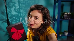 Joyful content creator holding present box, excited to do giveaway for subscribers. POV of media star happy to offer packed gift with ribbon to viewers, handheld camera shot