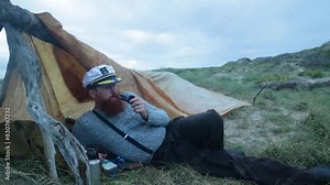 1900s sailor smoking a pipe by his makeshift camp along the coast.