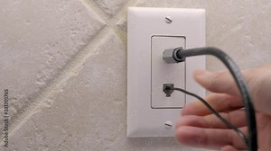 Male electrician plugging in landline telephone cord into wall mounted jack plate. Coax cable outlet and land line phone wall outlet. Stock Video