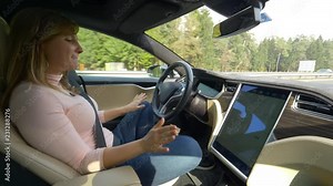 CLOSE UP: Cheerful Caucasian woman dancing in her cool autonomous car while driving down the highway. Carefree female tourist having fun during her road trip in a high tech self driving vehicle.