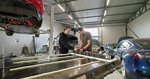 Two technicians working on repairing a lithium-ion battery pack for an electric vehicle in a modern car repair workshop. Electric car. Pack of battery cells module. EV car lithium-ion