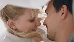 happy young couple lying in bed kissing under sheets sharing romantic...