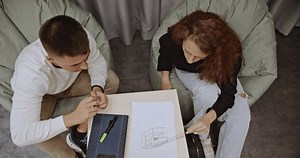 Two college students studying geometry together in comfortable beanbag chairs after class. They discuss formulas and practice problem-solving, showcasing teamwork and focused learning.